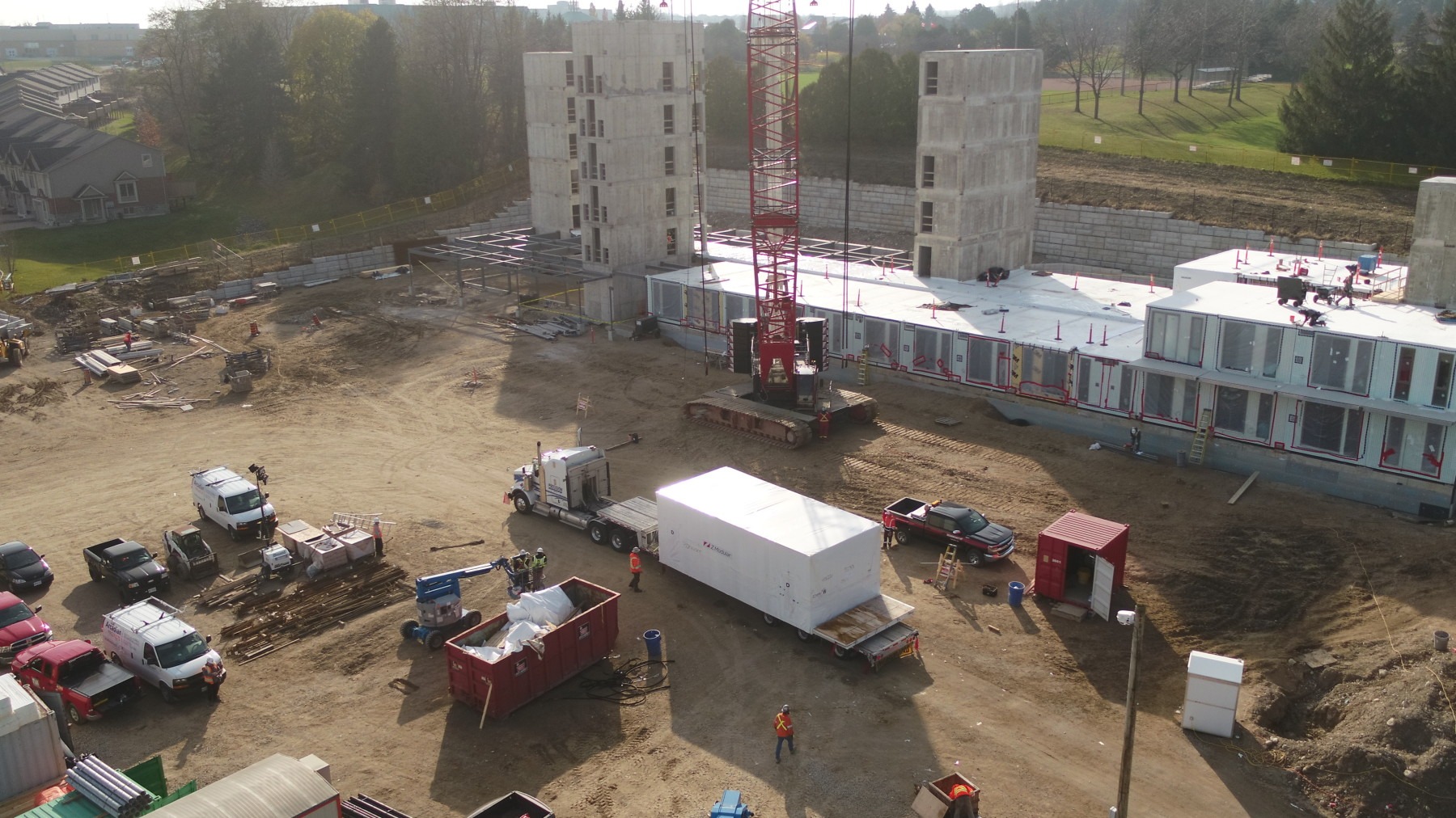 Construction site with a red crane, partially built structure, and various vehicles. Several people are working around the area. No landmarks visible.