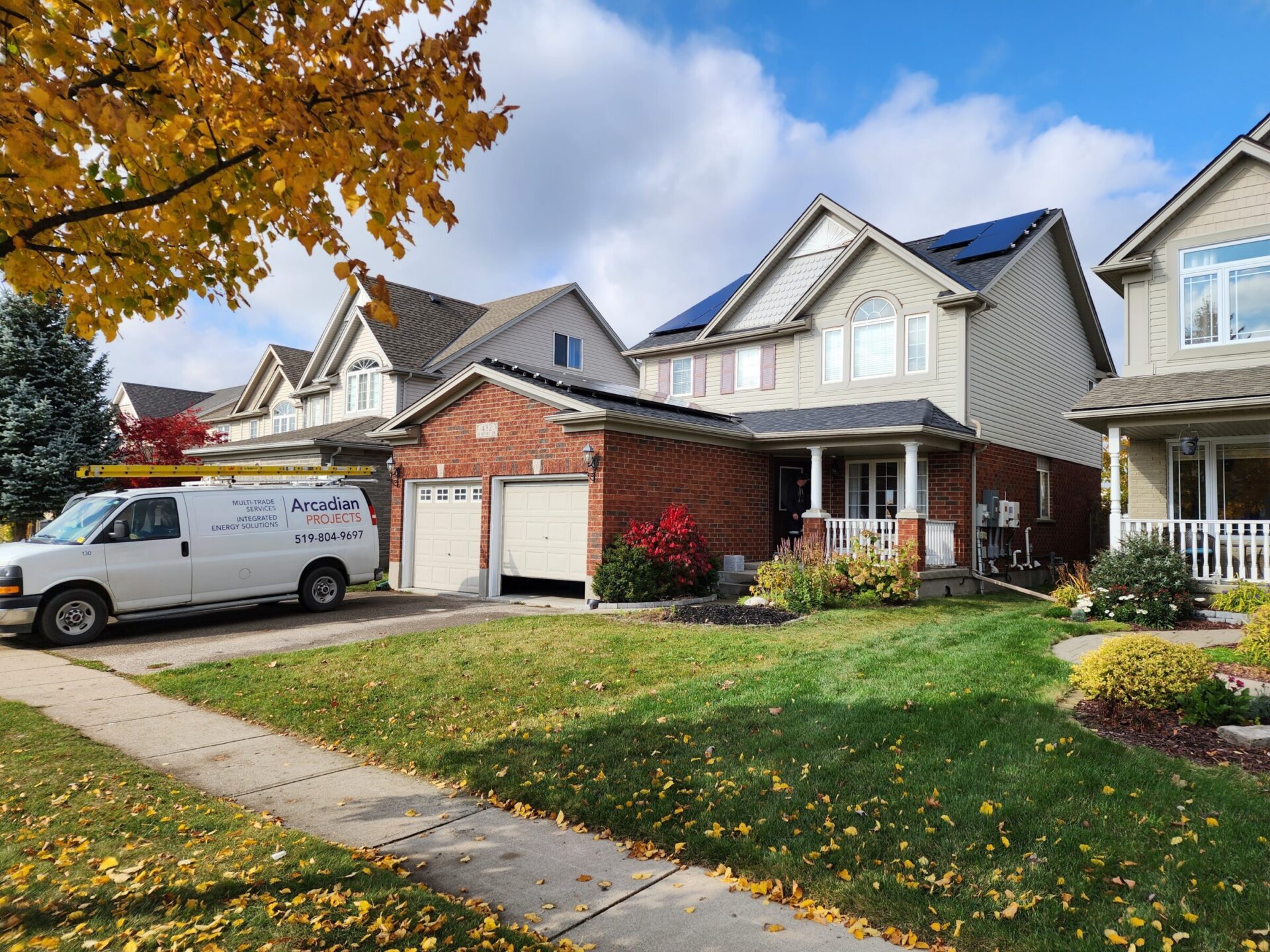 Suburban neighborhood with brick houses, well-kept lawns, and a sidewalk lined with trees. A white utility van is parked outside.