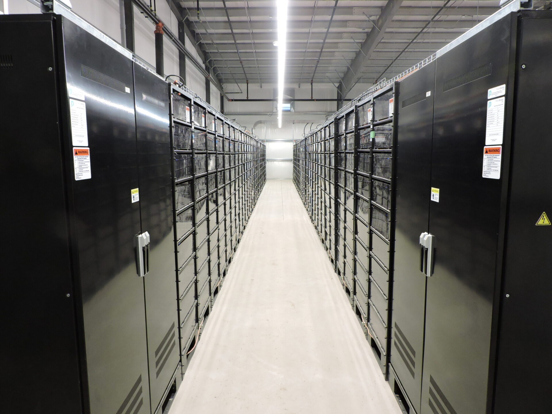 A spacious data center with rows of black server racks, lit by bright overhead lights, featuring clean and organized pathways between equipment.