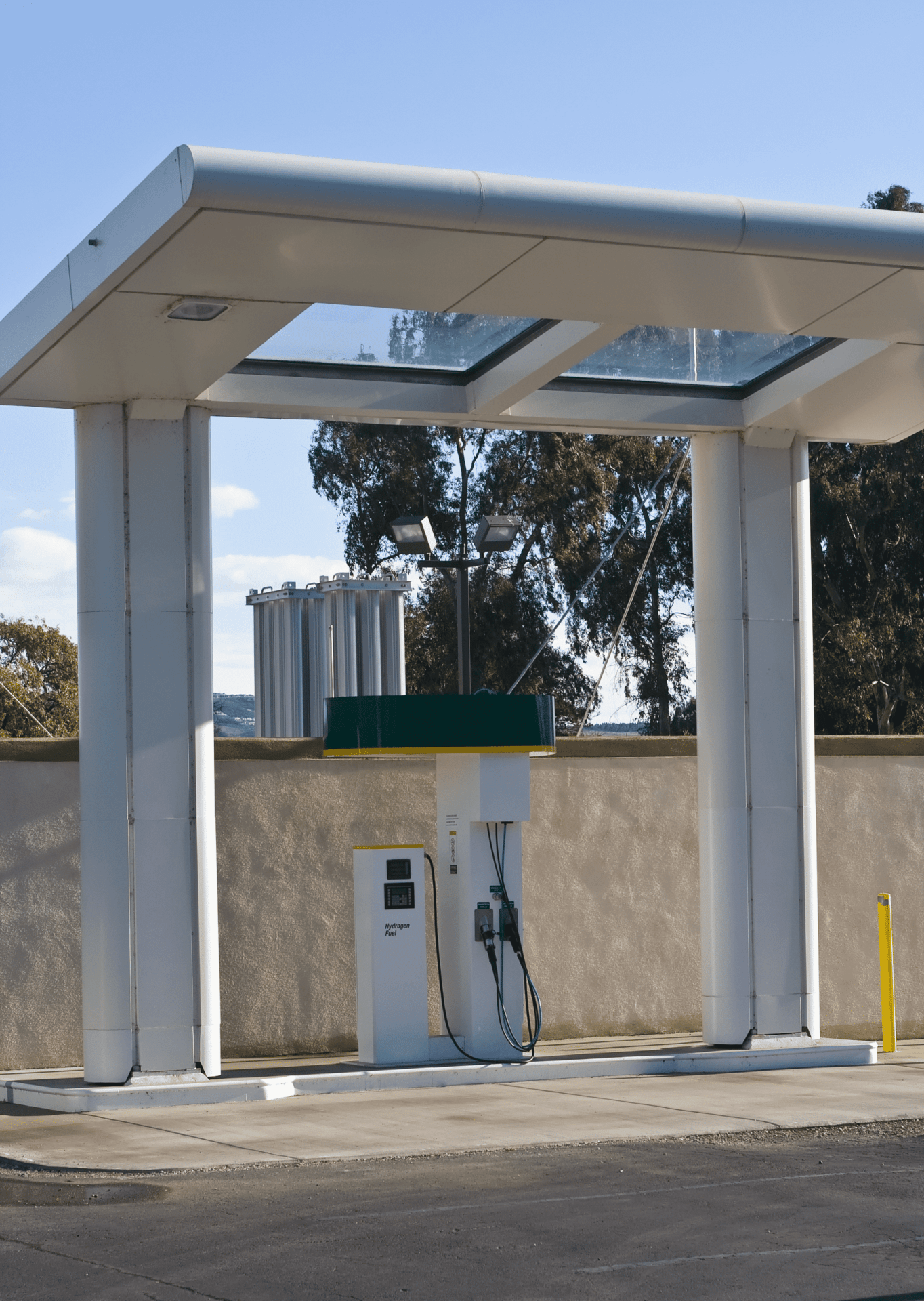 A modern hydrogen fuel station with a minimalist design, under a clear sky, surrounded by trees and concrete walls, empty of people.