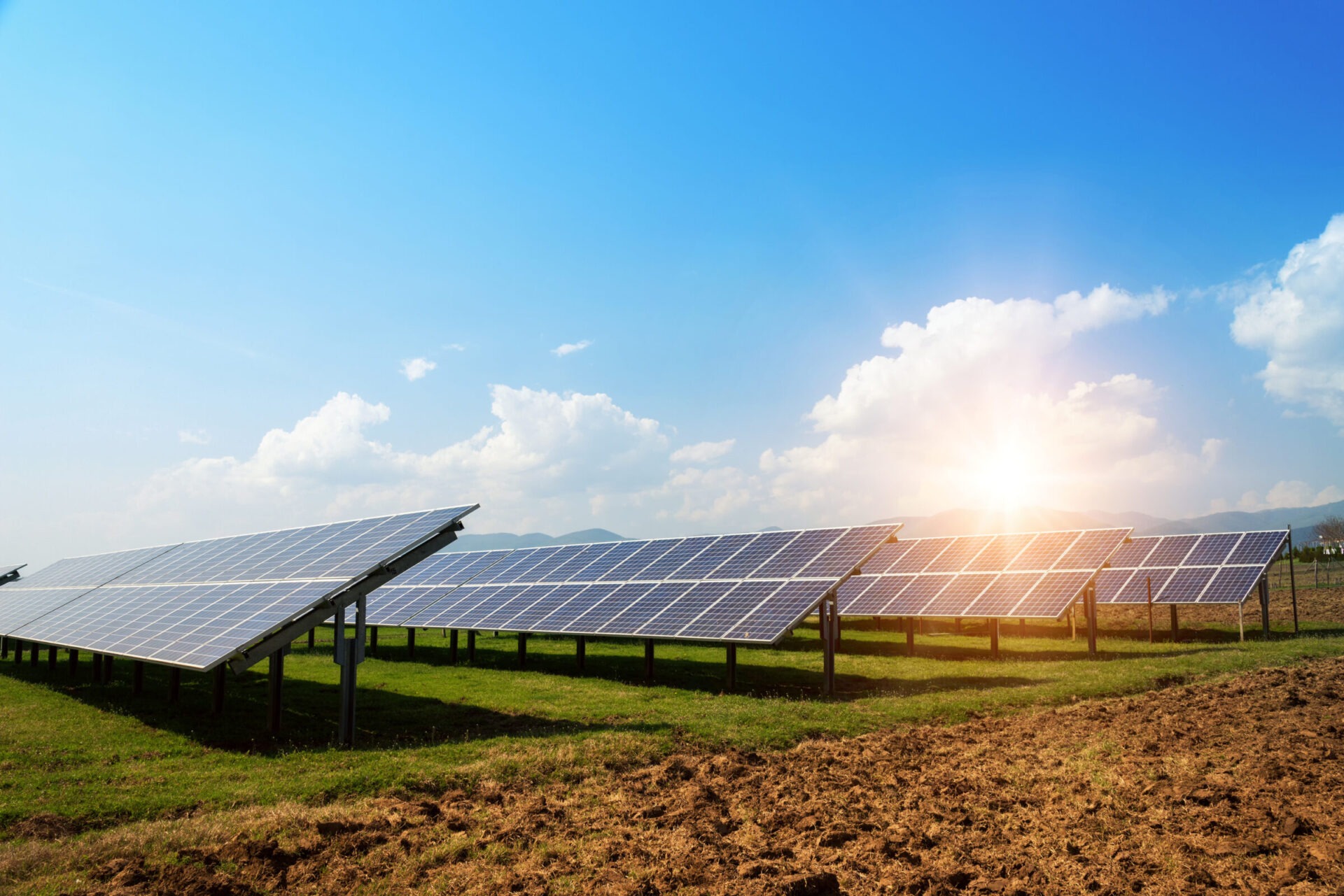 Solar panels set in a sunny, open field with clear blue skies and distant mountains, optimizing renewable energy collection from the sun's rays.